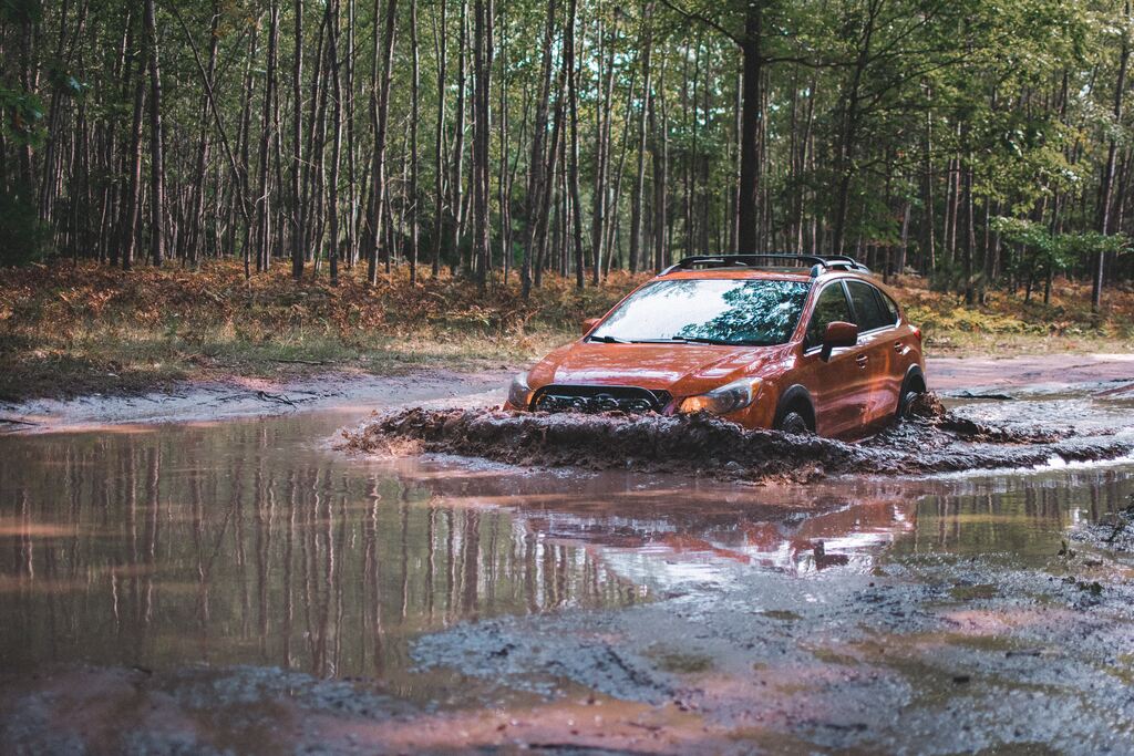 An orange Subaru Crosstrek trading through deep muddy water - a great example of why should you lift your car or suv?